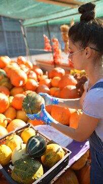 Amidst the market scene, a young female farmer is providing information on how they cultivate the pumpkins that are part of their offerings.