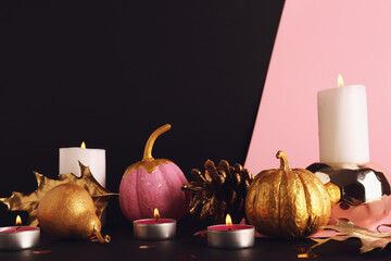 Painted pumpkins with golden pear, leaves and burning candles on colorful background