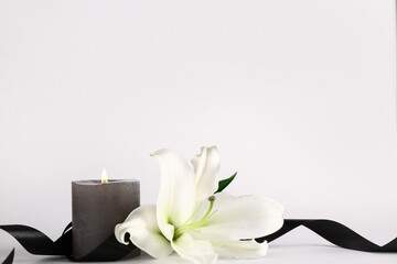 Beautiful lily with black ribbon and burning candle on white background