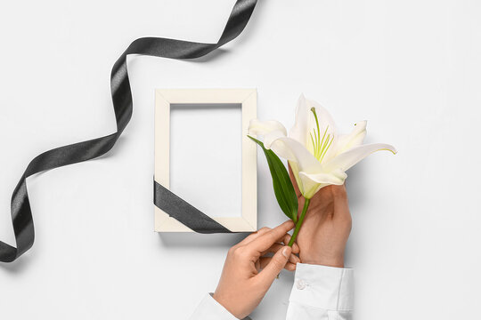 Female hands with lily flower, black ribbon and photo frame on white background