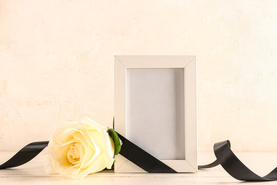 Photo frame with white rose and black ribbon on beige background
