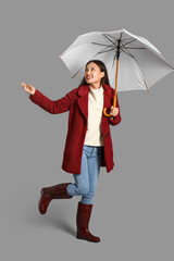 Beautiful young Asian woman with umbrella on grey background