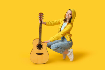 Pretty young woman with acoustic guitar on yellow background