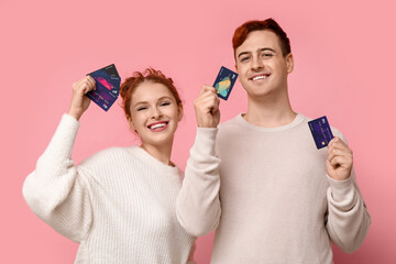 Young couple with credit cards on pink background