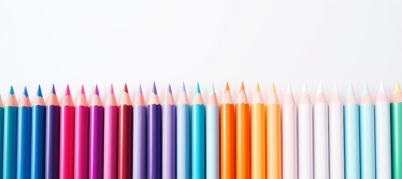 A row of colored pencils arranged in a rainbow gradient on a white background. This image shows a line of colored pencils with the tips pointing upwards. The colors range from pink to blue to orange