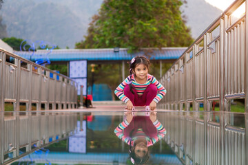 Asian child cute or kid girl happy smiling to sit squatting on skywalk bridge with reflection on...