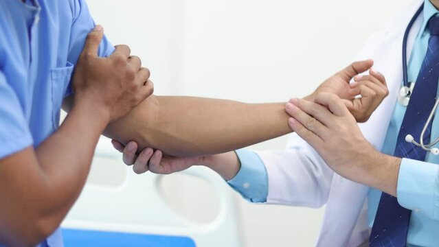 Doctor is diagnosing a male patient's arm and shoulder pain in a hospital examination room. Physical therapist testing patient's arm.