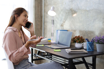 Female saleswoman in office using smartphone to send text messages online and using mobile phone to talk to customers.