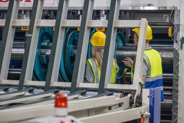 Techs inspecting, maintaining cardboard machine for safety, uninterrupted, high-quality production.