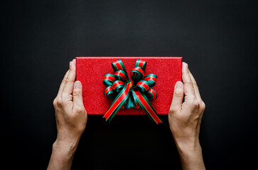 Hand holding red gift box with ribbon on black background for Boxing day and Black Friday shopping...