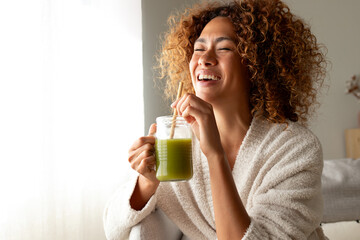 Happy multiracial woman enjoying healthy green juice at home. Female doing detox drinking green smoothie. Copy space. - obrazy, fototapety, plakaty