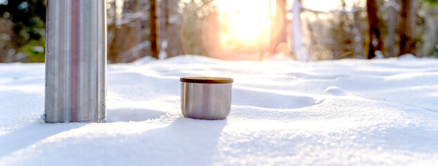 Metal thermos with a hot drink on the background of a winter mountain waterfall. Insulated drink...