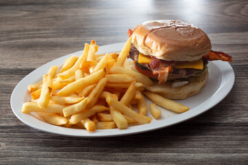 A view of a bacon cheeseburger with french fries.