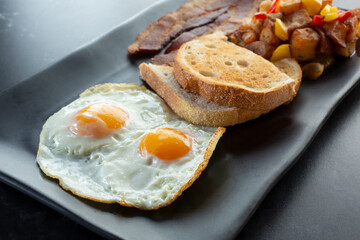 A view of a breakfast plate, featuring eggs, toast, bacon and potatoes.