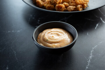 A view of a black plastic condiment cup of spicy mayo dipping sauce.