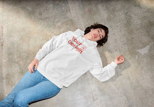 Mockup of woman wearing hoodie with customizable color, lying on floor