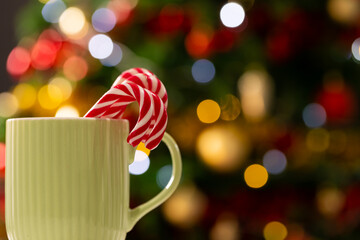 Mug with candy canes and christmas tree with fairy lights and copy space