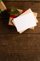 Vertical image of christmas gifts with decorations, white card and copy space on wooden background