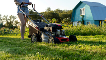 a girl mows the lawn with a lawn mower on a sunny day