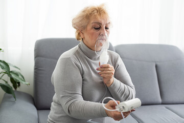Senior woman using a nebulizer makes inhalation at home and looks at the camera