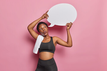 Athletic African American woman in black tracksuit holds empty speech bubble against pink backdrop...