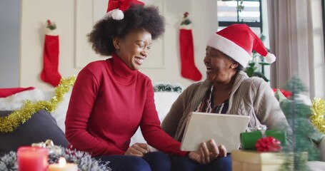 Happy african american mother and adult daughter in santa hats on christmas video call, slow motion - Powered by Adobe