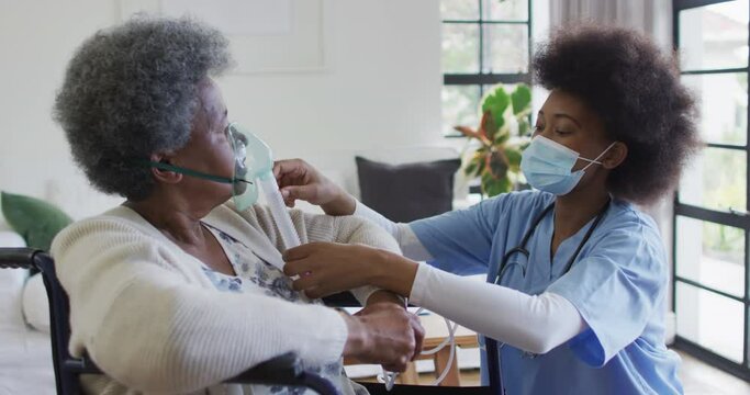 African american female doctor giving oxygen to senior female patient in wheelchair, slow motion