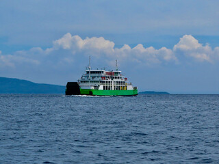 Cargo-passenger ferry on the open sea. A white and green cargo-passenger ferry moves along the sea on a cloudy day.