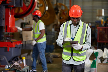 African factory worker or engineer writing on clipboard beside machine in the factory