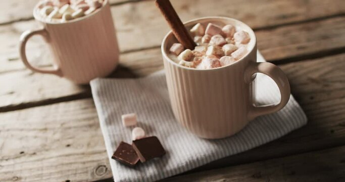 Video of mugs of chocolate with marshmallows, decorations and copy space on wooden background