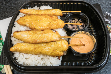 A take-out plastic container with Satay chicken
