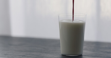 pour natural berry juice in organic yogurt in tumbler glass on black wood table with copy space