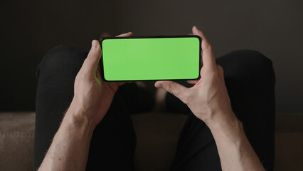 POV top view shot of man show phone with green screen indoor sitting on a couch