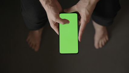 POV top view shot of man use phone with green screen indoor sitting on a couch
