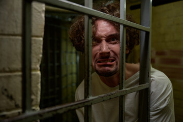 Portrait of crazy man with mad face crying bitterly in cage