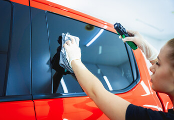 Car detailing worker cleaning and polishing car with microfiber cloth and vacuum.