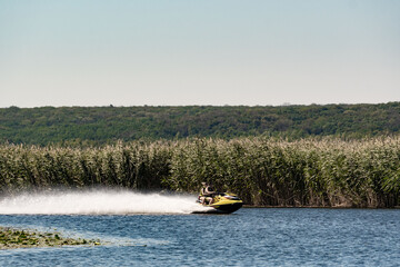 A large pond with clear water and green vegetation on the horizon. A picture of a water surface on which a jet ski rushes, raising splashes.