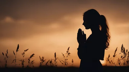 Fotobehang Silhouette of a praying girl with folded palms at sunset © Alernon77