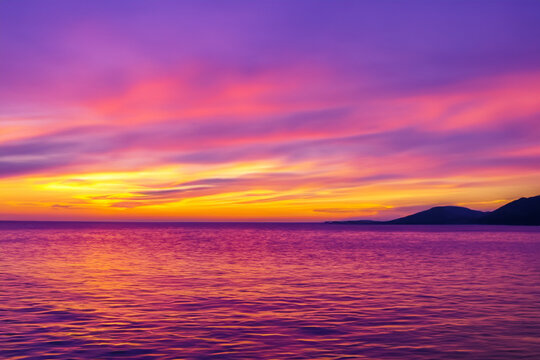 blue pink yellow sunset over the big ocean there are two big mountains in front. AI GENERATE