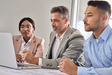 International diverse professional executives team workers or partners looking at laptop computer analyzing digital financial banking data corporate management working in office at group meeting.