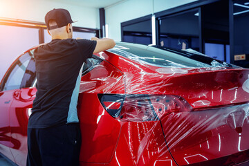 The process of installing protective film on the new red car. - obrazy, fototapety, plakaty