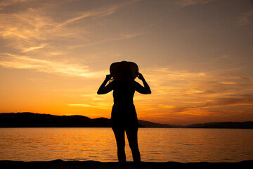woman in a hat against the background of the setting sun over the sea