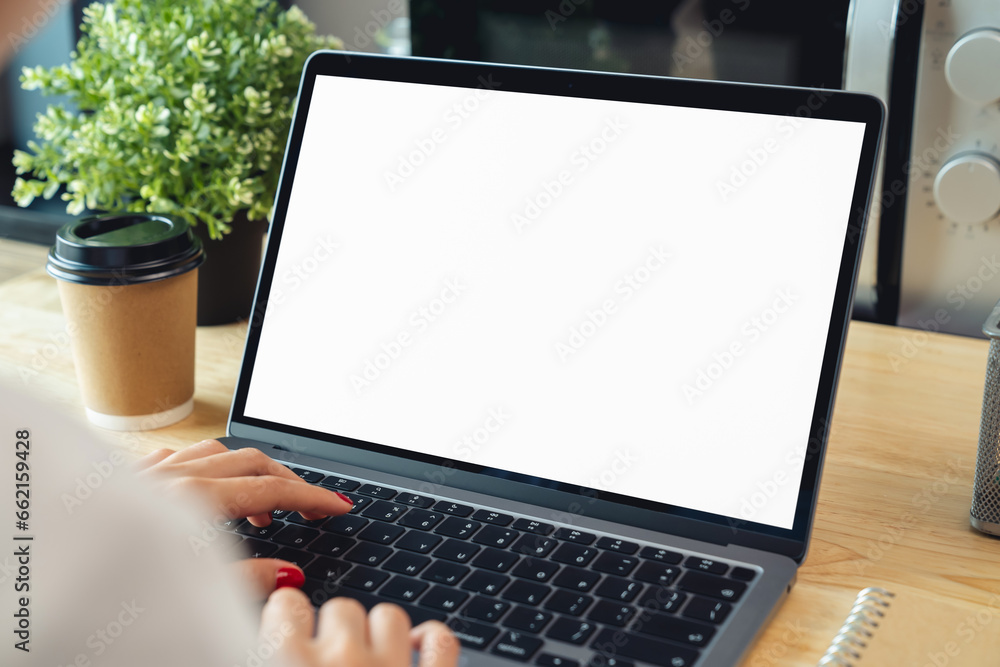 Sticker Woman hand using laptop and typing on keyboard with mockup of blank screen on wooden table.