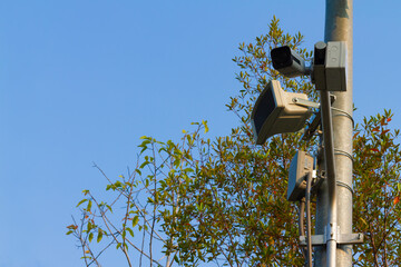 Low angle view of the surveillance security camera and loudspeaker on steel pole in outdoor public car parking with clear blue sky background.