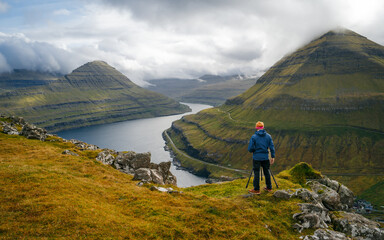 Fototapeta na wymiar A photographer with a camera on a viewpoint during an adventure in the Faroe Islands. Capturing moments of breathtaking beauty