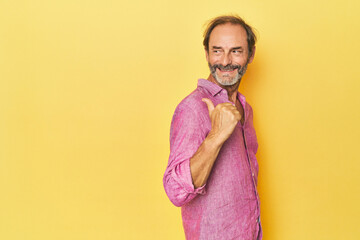 Obraz premium Caucasian middle-aged man in yellow studio points with thumb finger away, laughing and carefree.