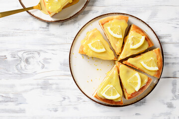 Sliced Fresh baked homemade lemon cheesecake with lemon curd and lemon slices.	white wooden...