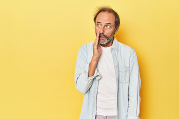 Caucasian middle-aged man in yellow studio is saying a secret hot braking news and looking aside