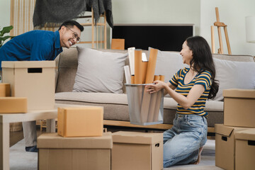 Young couple relaxing sitting on the floor around cardboard boxes at home, smiling happy moving to a new house.