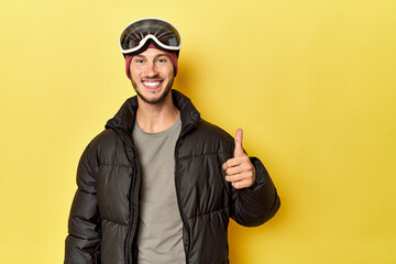 Obraz premium Man in winter coat with snow goggles on yellow smiling and raising thumb up